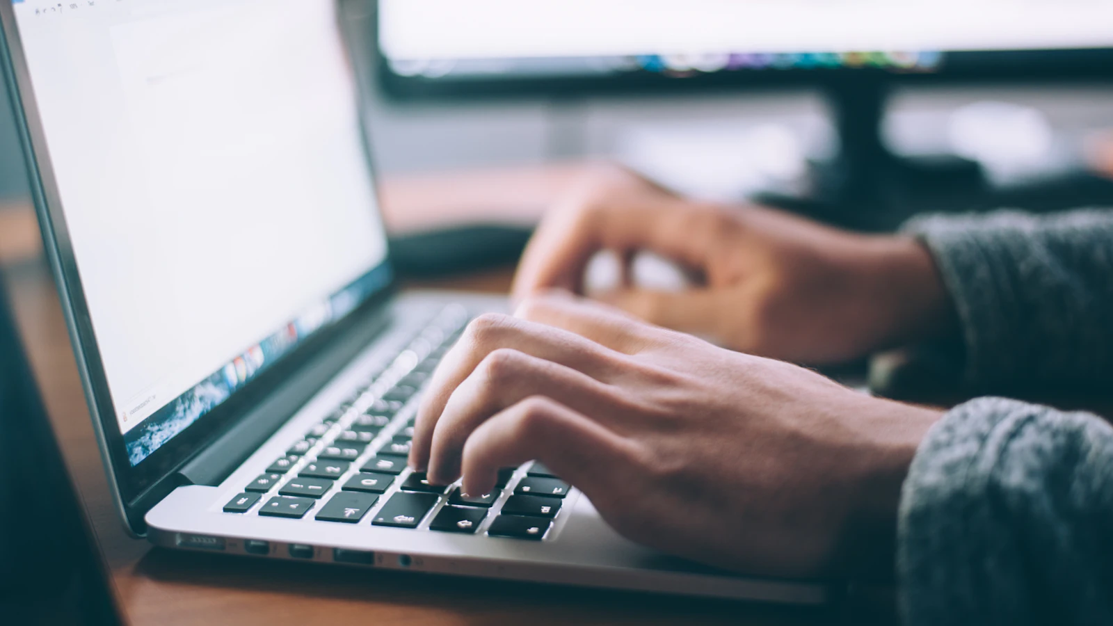 Close-up of a person's hands typing on a laptop keyboard at a desk